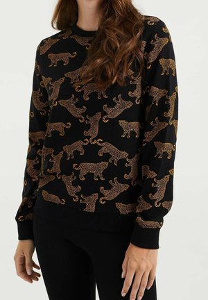 Femme portant un pull à manches longues noir avec un motif intégral de léopards orange et marron dans différentes poses.