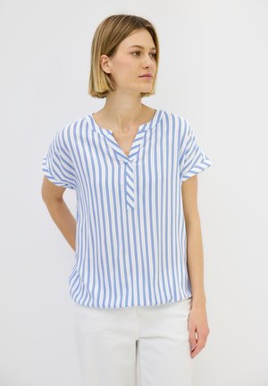 Blouse à manches courtes rayée bleue et blanche avec un décolleté en V et une coupe décontractée, fabriquée en tissu léger. Complétée par un pantalon blanc.