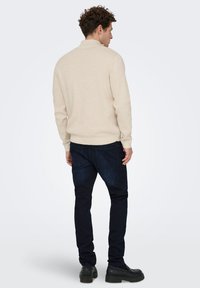 Beige sweater with a collar, textured fabric, long sleeves, paired with dark blue jeans and black shoes, viewed from the back.