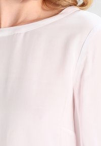 Blouse rose clair en tissu lisse et transparent. Dotée d'un grand col et de manches courtes, mettant en avant un design élégant et minimaliste.