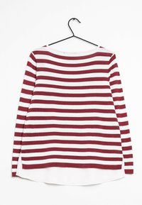 Pull à manches longues rayé rouge et blanc avec un col bateau, des fentes sur les côtés et un ourlet blanc sous le tissu rayé. Accroché à un crochet noir.