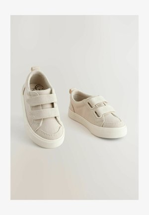 Beżowe sneakersy z płótna z podwójnymi rzepami, okrągłym noskiem i teksturowaną gumową podeszwą. Posiadają małą pętelkę z tyłu ułatwiającą zakładanie.