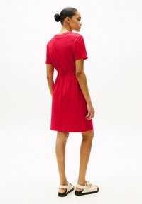 Vestito rosso a maniche corte con vita elastica, lunghezza al ginocchio, in morbido cotone con texture liscia, abbinato a sandali beige con cinturini regolabili.