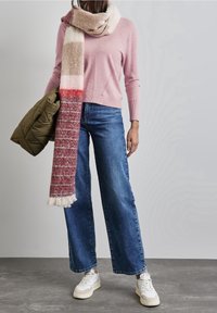 Ljusrosa tröja med långa ärmar, tillsammans med vida blå jeans. En flerfärgad stickad scarf och en olivgrön puffjacka. Vita sneakers.