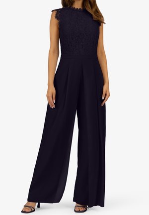 Mono negro con un cuerpo de encaje y un escote con un intrincado borde festoneado, pantalones de pierna ancha y una textura de tela suave.