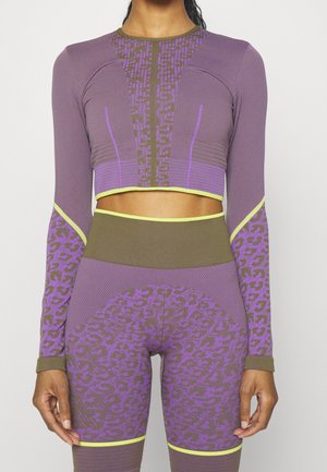 Femme portant un crop top violet et marron à manches longues et un legging taille haute avec accents imprimé animal et finition jaune, debout droite.