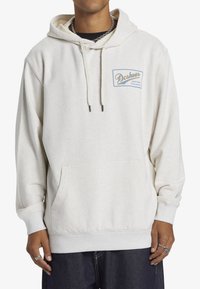 Light beige hoodie made of soft fabric, featuring a front pouch pocket and a small blue logo on the chest. Drawstring hood with silver tips.