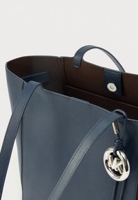 Modra torba za na rame iz usnja z gladko teksturo, z rjavim notranjim delom, zgornjimi ročaji za nošenje in srebrnim logotipom kot dodatkom iz kovine.