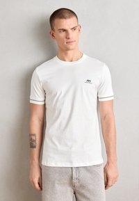T-shirt bianca con collo rotondo e maniche corte, caratterizzata da un bordo nero sulle maniche e un piccolo logo sul petto. Materiale in cotone morbido.