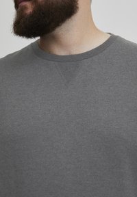 Sudadera gris de cuello redondo con tejido texturizado, sutiles detalles de costura y un ajuste relajado. Ideal para uso casual.