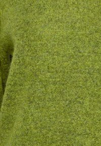 Grüner gestrickter Stoff mit einer weichen, strukturierten Oberfläche. Das Material wirkt flauschig mit einem melierten Muster, das hellere und dunklere Farbtöne kombiniert.