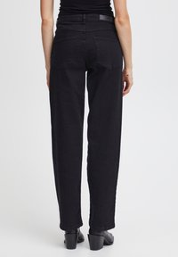 Jeans negros de cintura alta con un diseño de pierna recta, cinco bolsillos y detalles de costura sutiles, combinados con botas de tacón de tobillo negras.