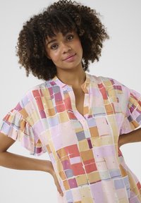 Korte mouw blouse van lichtgewicht stof, met een kleurrijk vierkant patroon en gouden accenten. Rimpels aan de mouwen en een kleine halslijn.