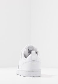 Scarpa sportiva bianca con colletto imbottito, parte superiore in sintetico liscia, linguetta sul tallone ben visibile e branding minimale. Suola liscia con un motivo di battistrada.