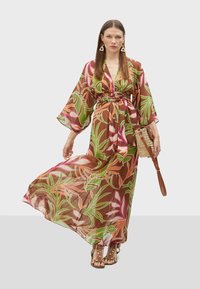 Robe maxi kimono en tissu transparent marron avec un motif floral rose et vert. Elle présente des manches larges, une taille nouée et une silhouette fluide.