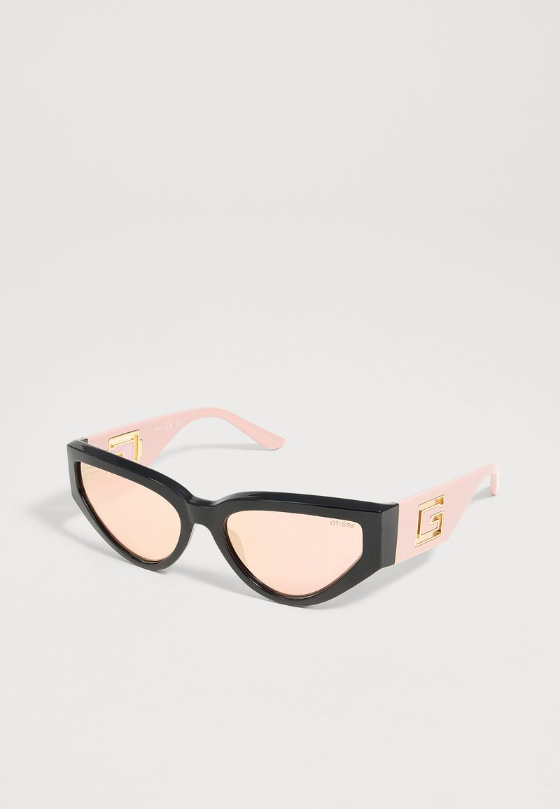 Lunettes de soleil œil de chat avec montures avant noires, branches rose clair et logo doré « G » sur les côtés.