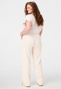 Lichtbeige wijde broek met een gladde textuur, heeft een middelhoge taille en achterzakken. Gecombineerd met een lichtgrijze kortärmelige top.