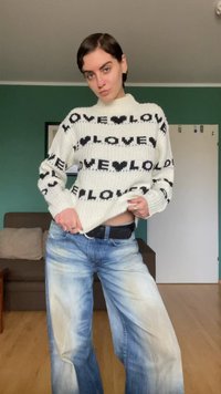 Υπερμεγέθη κρεμ πλεκτό πουλόβερ με μαύρο κείμενο "LOVE", σε συνδυασμό με ψηλόμεσα ανοιχτό μπλε τζιν με ξεβαμμένες λεπτομέρειες και άνετη εφαρμογή.