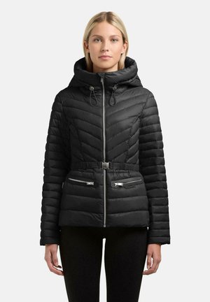 Vrouw die een zwart doorgestikt jack draagt met een hoge kraag, capuchon, verstelbare riem en een ritssluiting aan de voorkant en ritszakken, staand tegen een effen achtergrond.