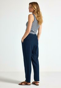 Pantaloni a sigaretta blu navy con tasche laterali, abbinati a un top a righe bianco e nero. La modella ha capelli mossi e indossa sandali marroni.