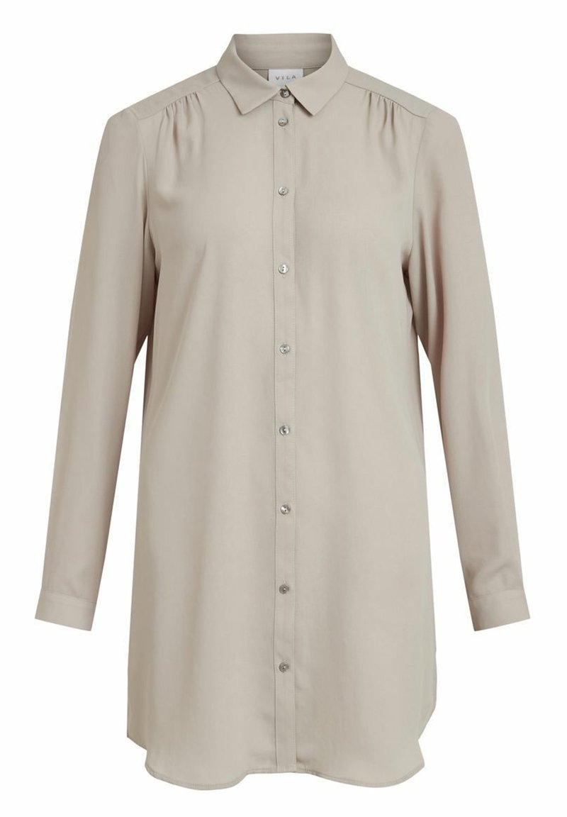 Camicia a maniche lunghe beige chiaro con colletto, chiusura a bottoni frontale e sottili pieghe sulle spalle. Tessuto liscio e orlo arrotondato.