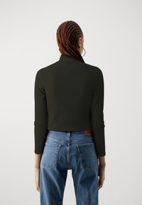 Person with braided hair wearing a black ribbed long-sleeve top and blue high-waisted jeans, shown from behind against white background.