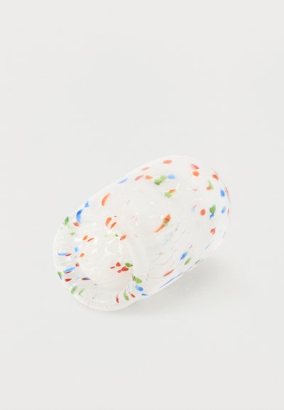 Διαφανές γυάλινο ποτήρι με διασκορπισμένες μικρές πολύχρωμες κουκκίδες σε κόκκινο, μπλε, πράσινο και πορτοκαλί πάνω σε λευκό φόντο, ξαπλωμένο στο πλάι.