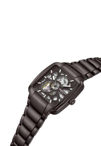 Reloj de acero inoxidable negro con una esfera esquelética cuadrada que revela engranajes, acentos plateados y una correa elegante y texturizada.