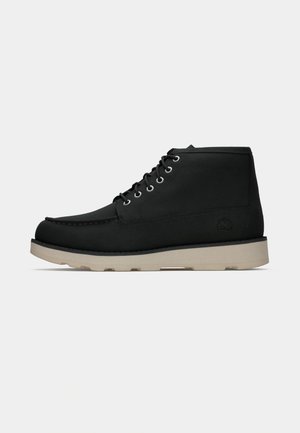 Black ankle boots featuring a suede upper, round toe, six metal eyelets, and a beige rubber sole with a textured pattern.
