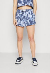 Námořnické a světle modré tie-dye šortky vyrobené z měkkého materiálu; mají elastický pás s bílou šňůrkou. V kombinaci s bílými teniskami.