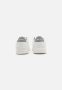 Hvite sneakers med en glatt skinnoverdel, grå detaljer på hælen og preget "HUGO" merke. Flat gummisåle.