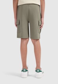 Olijfgroene cargoshorts met twee zijzakken, zachte stof en een relaxte pasvorm, gecombineerd met witte sneakers met groene accenten.