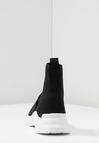 Černé pletené vysoké tenisky s texturovaným textilním svrškem, bílou gumovou podrážkou a malou poutkem na zadní části pro snadné obutí.