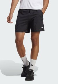 Pantalones cortos deportivos negros con cinturilla elástica, bolsillos laterales y un logo de Adidas en blanco. Combinados con calcetines blancos y zapatillas negras.