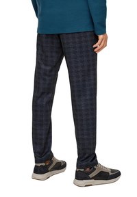 Donkerblauwe gestreepte broek van gestructureerde stof, gecombineerd met grijze en marineblauwe sneakers met vetersluiting en rubberen zolen.