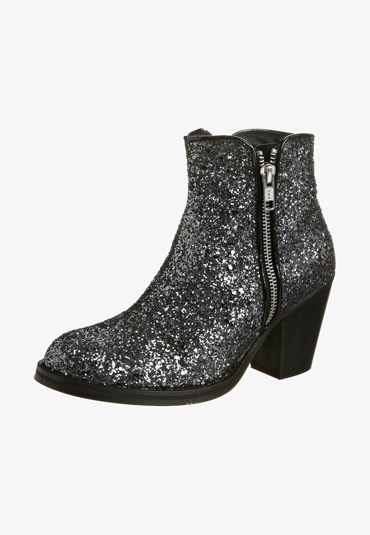 Bottine noire couverte de paillettes argentées avec fermeture éclair latérale et talon block, inclinée pour montrer le côté extérieur et la semelle.
