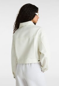 Witte cropped jack met een gestructureerde kraag, knoopmanchetten en een gladde textuur. Gecombineerd met lichtgrijze broeken.