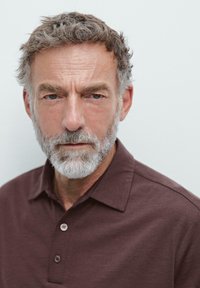 Mørkebrun polo shirt med korte ærmer, der har en krave og tre knapper. Personen har gråt hår og grå skæg.