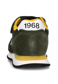 Vihreät samettikengät keltaisin yksityiskohdin, valkoinen kantapääosa, jossa on merkintä "1968", teksturoitu pinta ja kerrostettu valko-keltainen pohja.