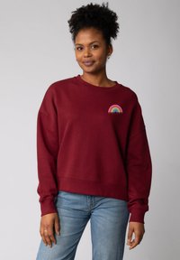 Bordeaux sweatshirt met een relaxte pasvorm en lange mouwen, voorzien van een regenboogontwerp en de tekst "WOMEN POWER" op de borst.