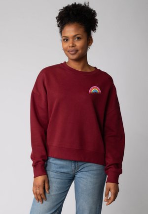 Bordeaux sweatshirt met een relaxte pasvorm en lange mouwen, voorzien van een regenboogontwerp en de tekst "WOMEN POWER" op de borst.