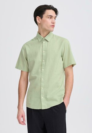 Short-sleeve shirt in light green cotton blend with a collared neck, button-down front, and subtle texture. Features a chest logo detail.