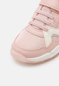 Rosa och vit sneakers med meshstruktur, snörning och vadderad sula, visad i närbild från en sned vinkel på en vit bakgrund.