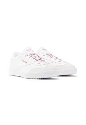 Par hvide lave Reebok-sneakers med lyserød branding og snørebånd, gummisåler og ruskind-tåhætte, vinklet mod højre på hvid baggrund.