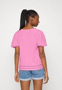 Blusa rosa de mangas curtas com decote redondo, apresentando um acabamento texturizado e detalhes na bainha. Combinada com calções de ganga azuis.