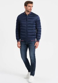 Navy Puffer-Jacke mit horizontalem Steppmuster, Frontreißverschluss, zwei seitlichen Taschen, gerippten Bündchen und Kragen mit kontrastierenden Besätzen.