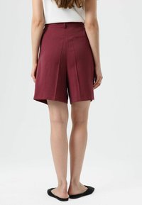 Bordeauxrode, op maat gemaakte korte broek met plooien, een vlakke tailleband en zijzakken. Glad oppervlak, kniehoogte, details met stiksels aan de zoom.