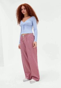 Hellblaues, geripptes Langarmshirt mit einer Vorderknotung, kombiniert mit rot-weiß karierten, weiten Hosen und weißen Sneakers.