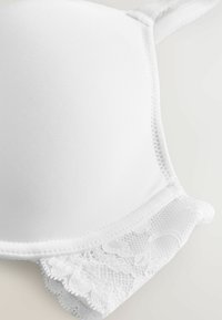 Soutien-gorge blanc en tissu lisse, avec des détails en dentelle au bas, et des bretelles réglables. Caractéristiques d'une forme arrondie sans coutures.