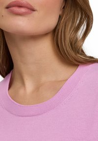 Maglione rosa chiaro con scollo rotondo e texture lavorata a maglia, che mostra sottili dettagli di cucitura intorno al colletto e all'area delle spalle.